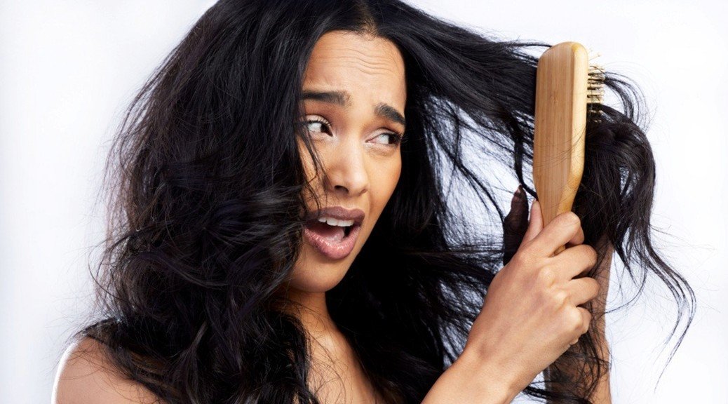 seorang wanita dengan rambut mengembang dan frizzy menggunakan serum rambut kering dari Kérastase